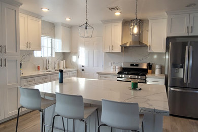 Example of a mid-sized minimalist l-shaped laminate floor and gray floor eat-in kitchen design in Orange County with an undermount sink, shaker cabinets, white cabinets, quartz countertops, white backsplash, quartz backsplash, stainless steel appliances, an island and white countertops