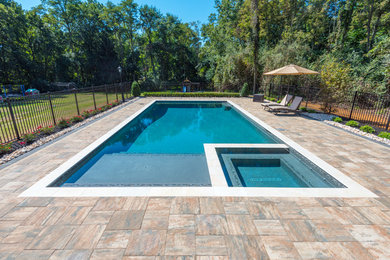 Large modern backyard rectangular lap pool in New York with a hot tub and brick pavers.