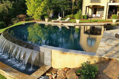Large trendy backyard stone and round infinity pool fountain photo in Birmingham