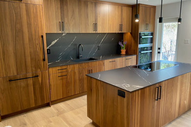 Enclosed kitchen - mid-sized 1960s light wood floor enclosed kitchen idea in Toronto with an undermount sink, flat-panel cabinets, medium tone wood cabinets, black backsplash, paneled appliances, an island and black countertops