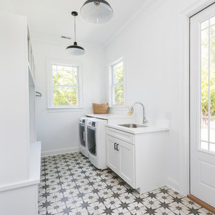 チャールストンの大きいカントリー風おしゃれな家事室 (アンダーカウンターシンク、白いキャビネット、クオーツストーンカウンター、白い壁、コンクリートの床、左右配置の洗濯機・乾燥機) の写真