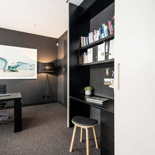 This is an example of a small modern study in Melbourne with black walls, carpet, a built-in desk and grey floors.