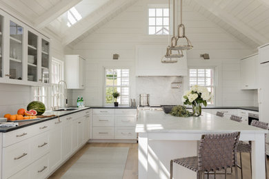 Beach style u-shaped light wood floor, beige floor, exposed beam, shiplap ceiling and vaulted ceiling kitchen photo in Other with an undermount sink, shaker cabinets, white cabinets, white backsplash, stainless steel appliances, an island, black countertops and stone slab backsplash
