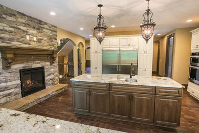 Example of a classic dark wood floor and brown floor kitchen design in Cleveland with an undermount sink, raised-panel cabinets, white cabinets, granite countertops, beige backsplash, travertine backsplash, stainless steel appliances, an island and white countertops