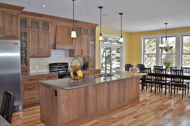 Example of a transitional light wood floor eat-in kitchen design in Other with an undermount sink, shaker cabinets, medium tone wood cabinets, granite countertops, black backsplash, porcelain backsplash, stainless steel appliances and an island