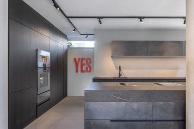 Immagine di una grande cucina moderna con ante lisce, ante nere, elettrodomestici in acciaio inossidabile, top nero, lavello integrato e pavimento in cemento