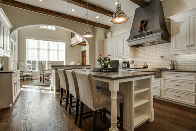 Design ideas for a mid-sized arts and crafts u-shaped separate kitchen in Dallas with recessed-panel cabinets, white cabinets, solid surface benchtops, white splashback, brick splashback, white appliances, dark hardwood floors, with island, brown floor, a farmhouse sink and black benchtop.