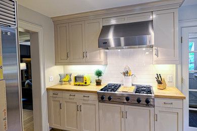 Example of a mid-sized farmhouse u-shaped light wood floor and beige floor eat-in kitchen design in New York with a farmhouse sink, shaker cabinets, beige cabinets, soapstone countertops, white backsplash, ceramic backsplash, stainless steel appliances and a peninsula