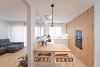 バルセロナにある中くらいな北欧スタイルのおしゃれなキッチン (アンダーカウンターシンク、淡色木目調キャビネット、白いキッチンパネル、黒い調理設備、ラミネートの床、白いキッチンカウンター) の写真