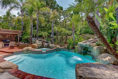 Large trendy backyard stone and round aboveground hot tub photo in Orange County