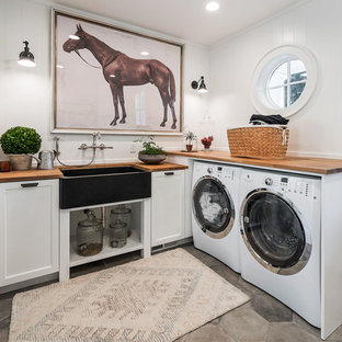 Design ideas for a country l-shaped utility room in Portland with a belfast sink, recessed-panel cabinets, white cabinets, wood worktops, a side by side washer and dryer, grey floors and brown worktops.