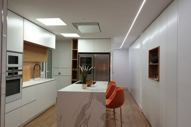 Diseño de cocina lineal moderna abierta con armarios con paneles lisos, puertas de armario blancas, encimera de laminado, una isla y encimeras blancas