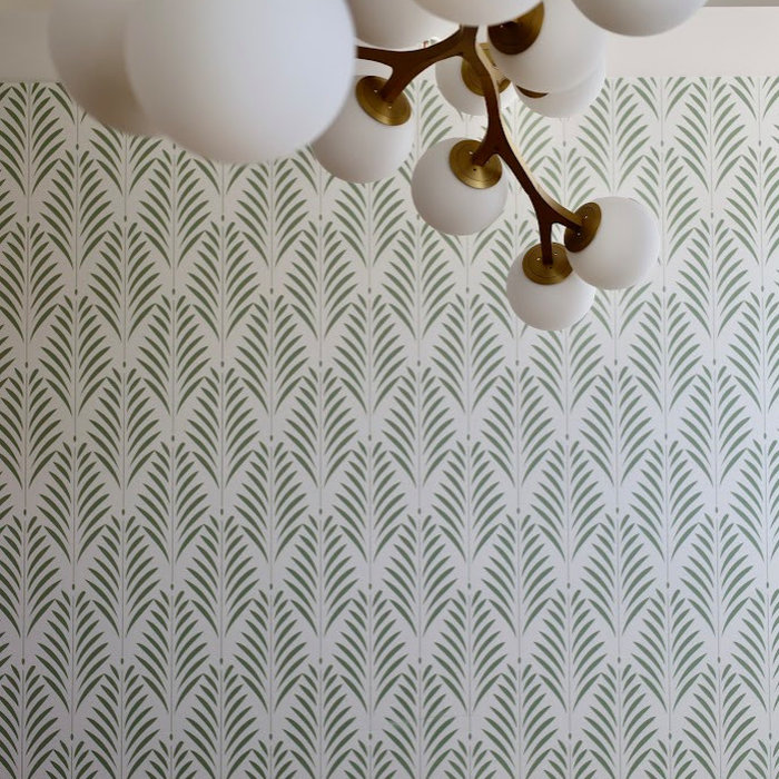 This modern dining room features a stunning geometric wallpaper in muted green, adding depth and texture to the space while reflecting nature-inspired design. A set of vintage-style cane dining chairs