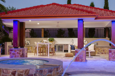 Large country backyard patio in Brisbane with an outdoor kitchen, natural stone pavers and a pergola.