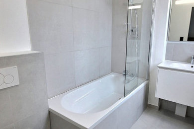Aménagement d'une salle de bain principale moderne de taille moyenne avec des portes de placard blanches, une baignoire encastrée, un combiné douche/baignoire, WC suspendus, un carrelage gris, des carreaux de céramique, un mur blanc, un sol en carrelage de céramique, un lavabo suspendu, un sol gris, aucune cabine, un plan de toilette blanc, une fenêtre, meuble simple vasque et meuble-lavabo suspendu.