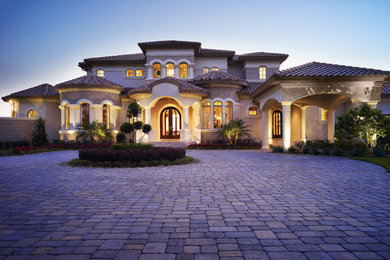Inspiration for a huge mediterranean beige two-story stucco house exterior remodel in Tampa with a hip roof and a tile roof