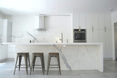 Example of a mid-sized trendy u-shaped cement tile floor and gray floor open concept kitchen design in Orange County with flat-panel cabinets, quartz countertops, white backsplash, marble backsplash, stainless steel appliances, an island, a drop-in sink and white cabinets