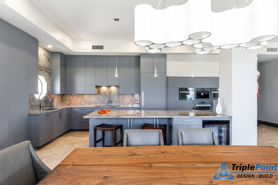 Example of a large trendy l-shaped porcelain tile, beige floor, tray ceiling and vaulted ceiling open concept kitchen design in Tampa with an undermount sink, flat-panel cabinets, gray cabinets, granite countertops, gray backsplash, granite backsplash, stainless steel appliances, an island and gray countertops