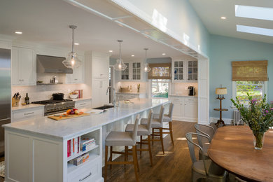 Example of a huge classic l-shaped medium tone wood floor eat-in kitchen design in Philadelphia with a farmhouse sink, recessed-panel cabinets, white cabinets, marble countertops, white backsplash, glass tile backsplash, stainless steel appliances and an island