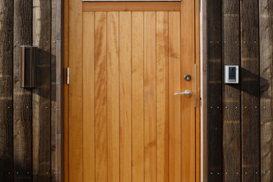 Ejemplo de puerta principal de estilo de casa de campo grande con paredes negras, suelo de cemento, puerta simple, puerta marrón, suelo gris y madera