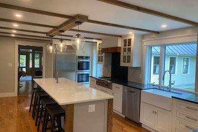 Example of a mid-sized cottage medium tone wood floor and exposed beam kitchen design in Other with shaker cabinets, white cabinets, ceramic backsplash and black countertops