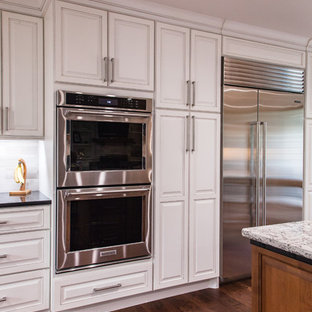 Пример оригинального дизайна: большая параллельная кухня в стиле современная классика с кладовкой, врезной раковиной, фасадами с выступающей филенкой, белыми фасадами, столешницей из кварцита, разноцветным фартуком, фартуком из известняка, техникой из нержавеющей стали, паркетным полом среднего тона, островом и коричневым полом