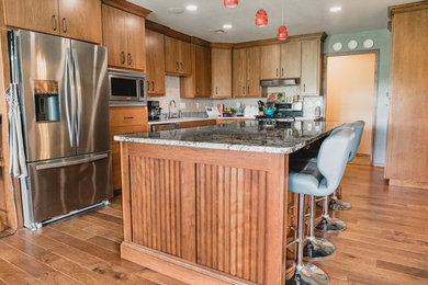 Open concept kitchen - large traditional l-shaped medium tone wood floor and brown floor open concept kitchen idea in Oklahoma City with flat-panel cabinets, medium tone wood cabinets, granite countertops, an island, gray countertops, an undermount sink, beige backsplash, stainless steel appliances and ceramic backsplash