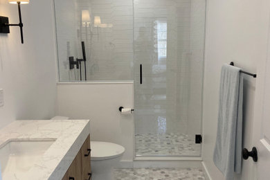 Inspiration for a mid-sized white tile and porcelain tile marble floor, gray floor and single-sink alcove shower remodel in New York with flat-panel cabinets, medium tone wood cabinets, a bidet, gray walls, an undermount sink, quartzite countertops, a hinged shower door and a freestanding vanity