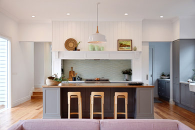 Inspiration for a large traditional galley open plan kitchen in Melbourne with a farmhouse sink, shaker cabinets, grey cabinets, quartz benchtops, white splashback, ceramic splashback, stainless steel appliances, light hardwood floors and with island.