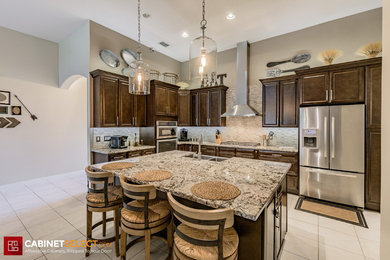Large trendy l-shaped porcelain tile and beige floor eat-in kitchen photo in Orlando with a farmhouse sink, dark wood cabinets, granite countertops, beige backsplash, stone tile backsplash, stainless steel appliances, an island and beige countertops