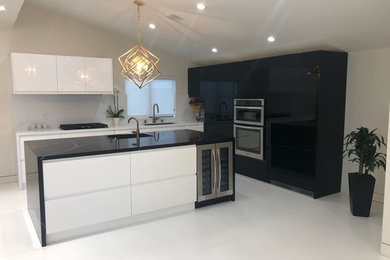 Example of a large minimalist l-shaped white floor kitchen design in Los Angeles with flat-panel cabinets, white cabinets, marble countertops, white backsplash, stainless steel appliances, an island and black countertops