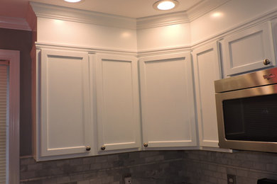 Mid-sized elegant l-shaped light wood floor eat-in kitchen photo in Manchester with a drop-in sink, recessed-panel cabinets, white cabinets, laminate countertops, gray backsplash, stone tile backsplash, stainless steel appliances and an island