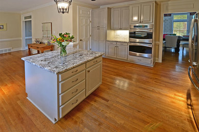 Example of a large classic u-shaped light wood floor eat-in kitchen design in Other with raised-panel cabinets, white cabinets, granite countertops, white backsplash, subway tile backsplash, stainless steel appliances, an island and a farmhouse sink