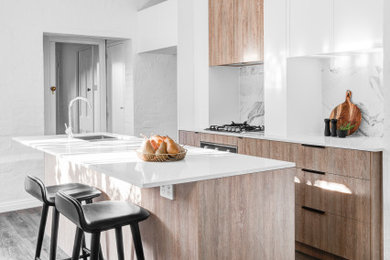 Design ideas for a traditional kitchen in Other with a double-bowl sink, flat-panel cabinets, light wood cabinets, quartz benchtops, white splashback, porcelain splashback, stainless steel appliances, vinyl floors, with island, brown floor and white benchtop.