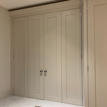 Dark blue kitchen island with neutral coloured cabinets and full length larder