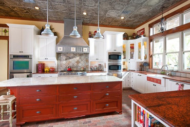 Country l-shaped kitchen in Dallas with a farmhouse sink, shaker cabinets, red cabinets, multi-coloured splashback, stainless steel appliances, with island and multi-coloured floor.