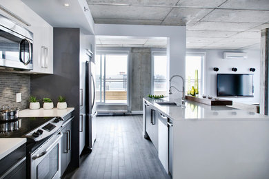 Small modern single-wall open plan kitchen in Montreal with with island, an undermount sink, flat-panel cabinets, white cabinets, quartz benchtops, grey splashback, stainless steel appliances and dark hardwood floors.