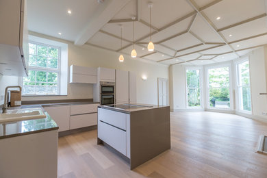 Large eclectic l-shaped eat-in kitchen in Other with an integrated sink, flat-panel cabinets, white cabinets, white splashback, light hardwood floors, with island and white floor.