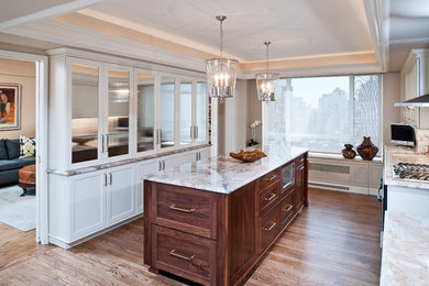 Photo of a large contemporary galley eat-in kitchen in New York with an undermount sink, recessed-panel cabinets, white cabinets, white splashback, matchstick tile splashback, stainless steel appliances, light hardwood floors and with island.