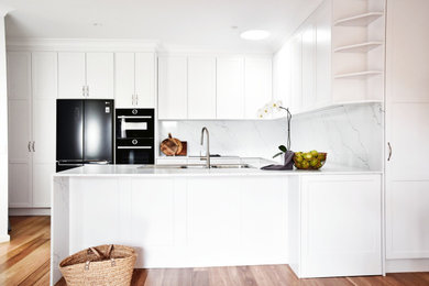Inspiration for a mid-sized traditional u-shaped eat-in kitchen in Canberra - Queanbeyan with a double-bowl sink, shaker cabinets, white cabinets, quartz benchtops, white splashback, engineered quartz splashback, black appliances, medium hardwood floors, a peninsula, brown floor and white benchtop.
