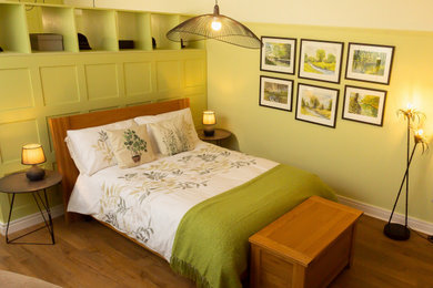 Diseño de dormitorio principal y blanco de tamaño medio con paredes verdes, suelo laminado y suelo marrón
