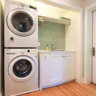 Design ideas for a small contemporary single-wall laundry cupboard in DC Metro with a submerged sink, flat-panel cabinets, beige cabinets, engineered stone countertops, green walls, light hardwood flooring, a stacked washer and dryer, brown floors and beige worktops.