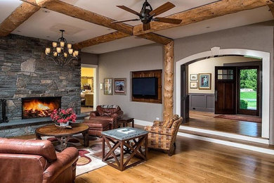 Example of a large mountain style formal and enclosed medium tone wood floor living room design in New York with gray walls, a standard fireplace, a stone fireplace and a wall-mounted tv