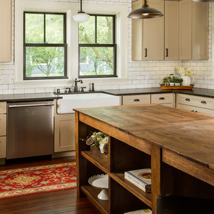 This is an example of a large country l-shaped kitchen pantry in Minneapolis with a farmhouse sink, shaker cabinets, beige cabinets, soapstone benchtops, white splashback, subway tile splashback, stainless steel appliances, medium hardwood floors, with island and brown floor.