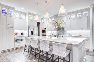 Example of a transitional l-shaped dark wood floor and brown floor kitchen design in Dallas with recessed-panel cabinets, white cabinets, stainless steel appliances, an island and white countertops