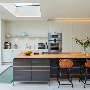 Modelo de cocina lineal, contemporánea, de tamaño medio, abierta, con fregadero bajoencimera, armarios con paneles lisos, puertas de armario blancas, encimera de cuarcita, electrodomésticos de acero inoxidable, suelo de azulejos de cemento, una isla, suelo gris, encimeras blancas y salpicadero blanco