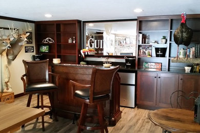 Example of a large classic galley light wood floor seated home bar design in Other with an undermount sink, recessed-panel cabinets, dark wood cabinets, granite countertops, black backsplash and stone slab backsplash