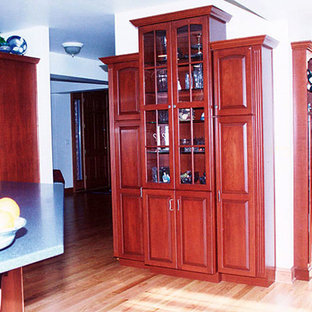 Idée de décoration pour une arrière-cuisine linéaire avec un placard à porte vitrée, des portes de placard en bois sombre, un sol en bois clair et un îlot central.