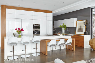 Large minimalist l-shaped concrete floor and brown floor open concept kitchen photo with white cabinets, gray backsplash, glass sheet backsplash, paneled appliances, an island, flat-panel cabinets, an undermount sink, quartz countertops and white countertops