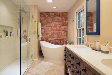Photo of a mid-sized industrial master bathroom in DC Metro with furniture-like cabinets, brown cabinets, a freestanding tub, a corner shower, a two-piece toilet, beige tile, ceramic tile, beige walls, porcelain floors, an undermount sink, engineered quartz benchtops, grey floor, a hinged shower door and beige benchtops.